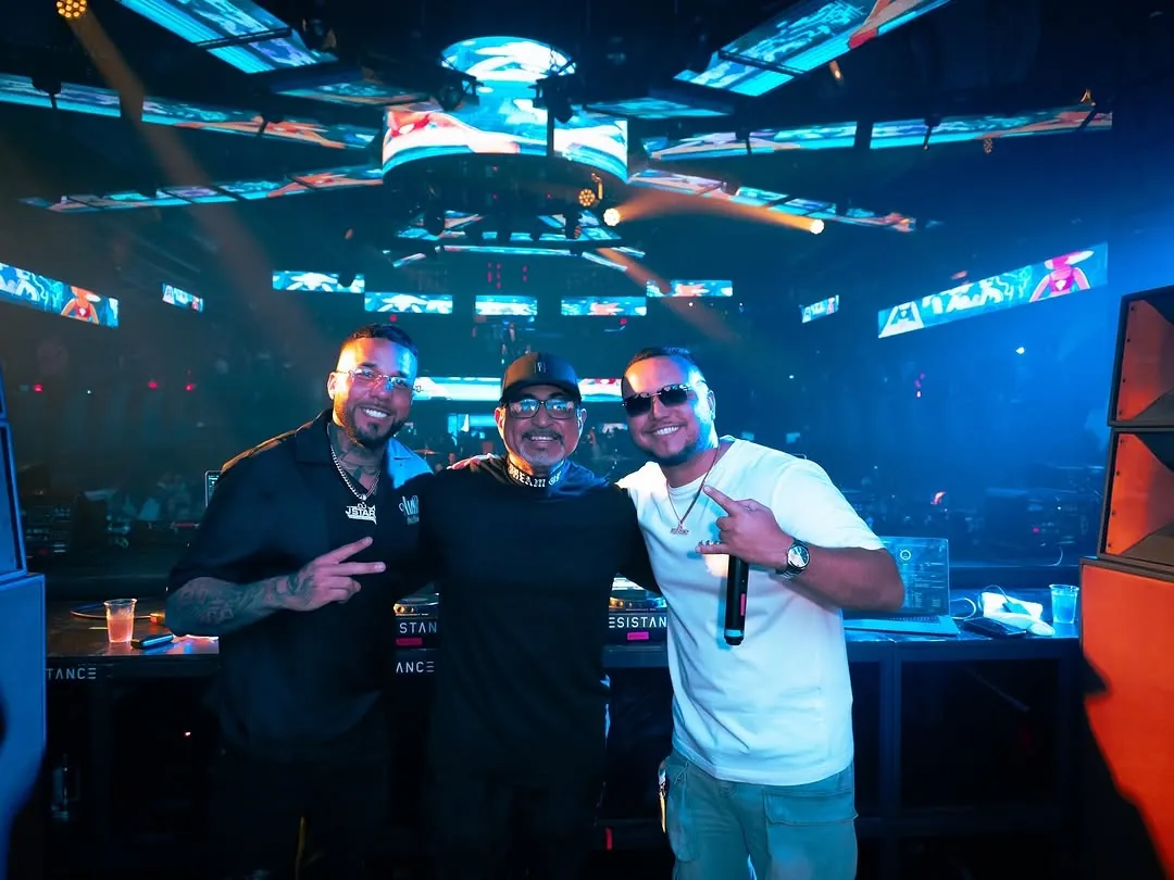 DJ Caises performing on stage with two other performers. Opens larger.